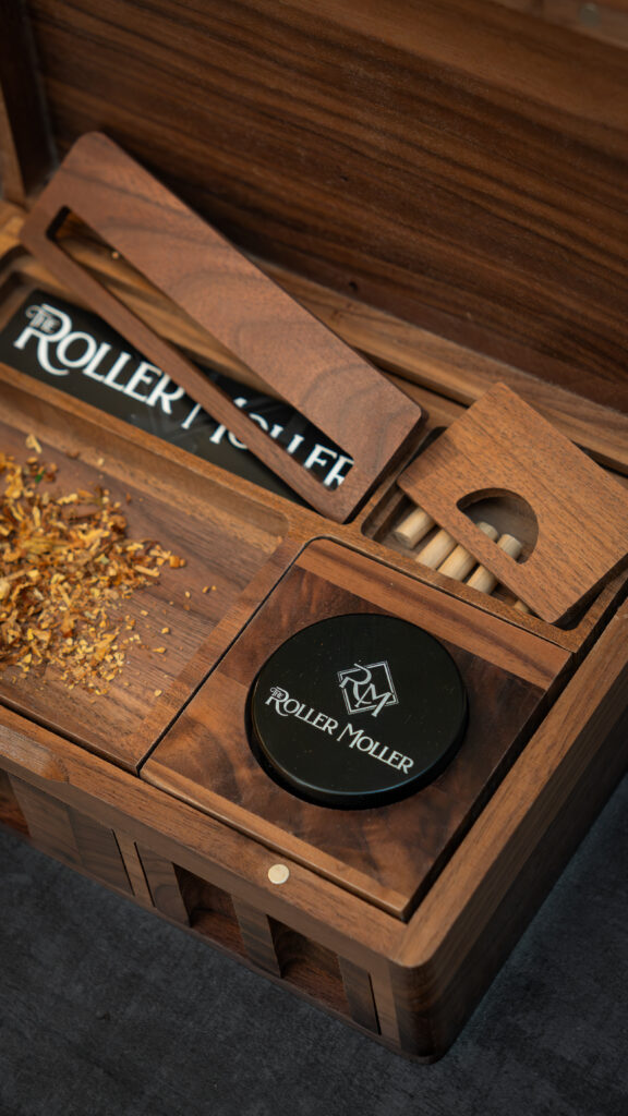 Close-up of an open wooden box with a black grinder, lifted compartment covers and dried material on the tray.